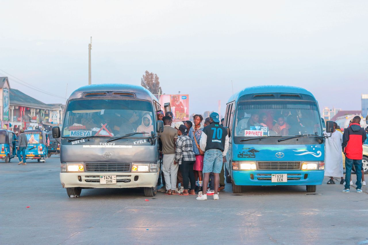 People gathering at a busy bus station in an urban area, boarding vehicles for travel.