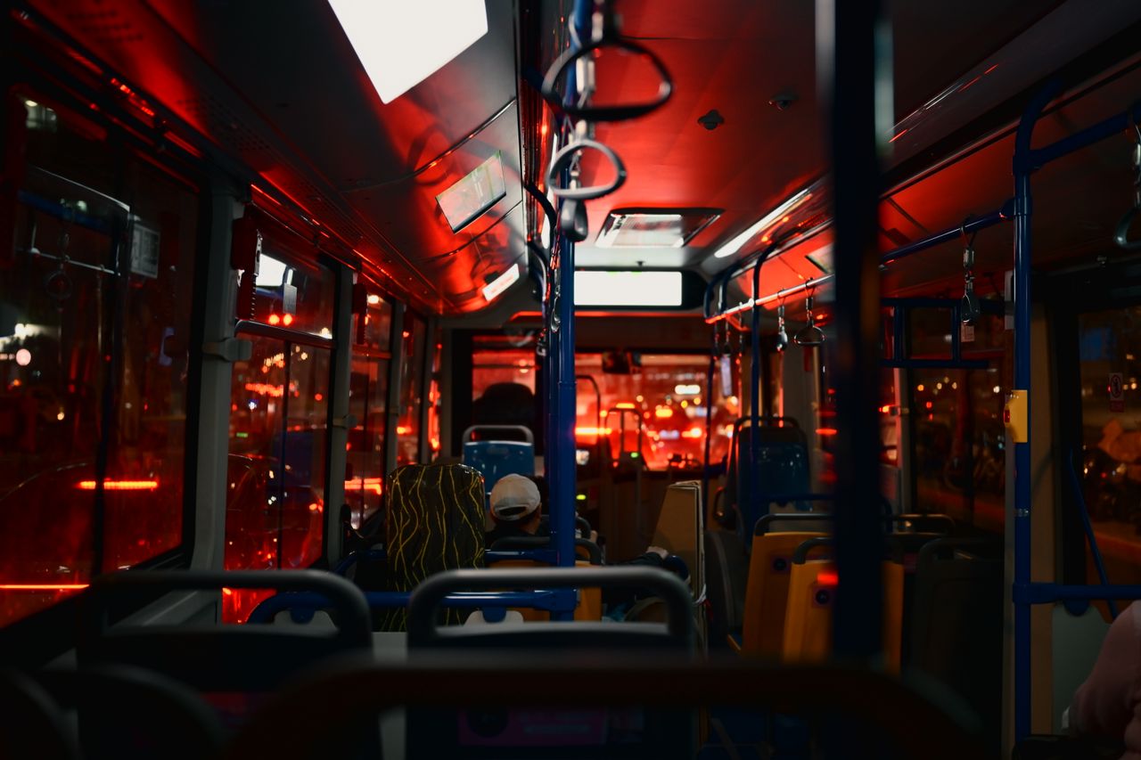 Nighttime city bus interior with passengers, illuminated by red lights, creating a moody atmosphere.